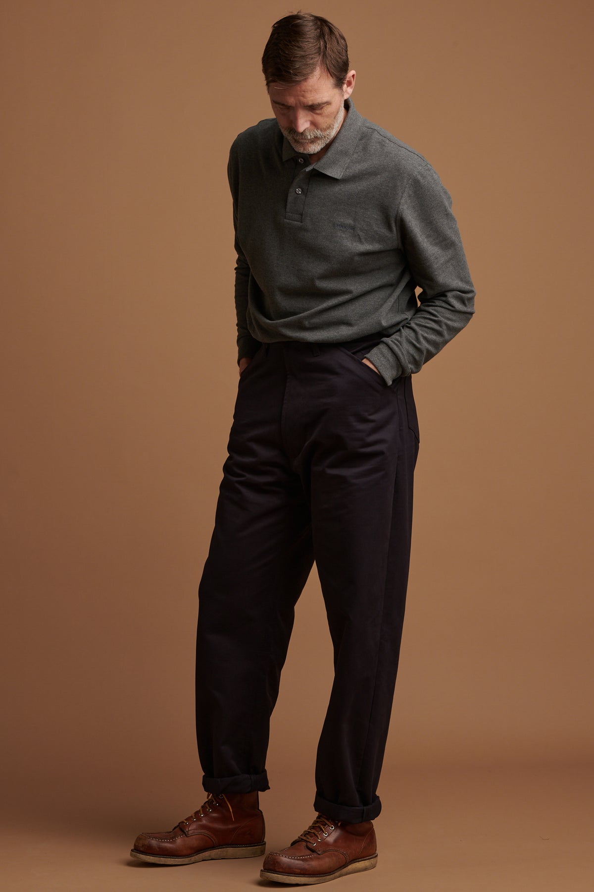 Patrick looking down, wearing cotton chore trousers in navy with his hands in the front pockets.