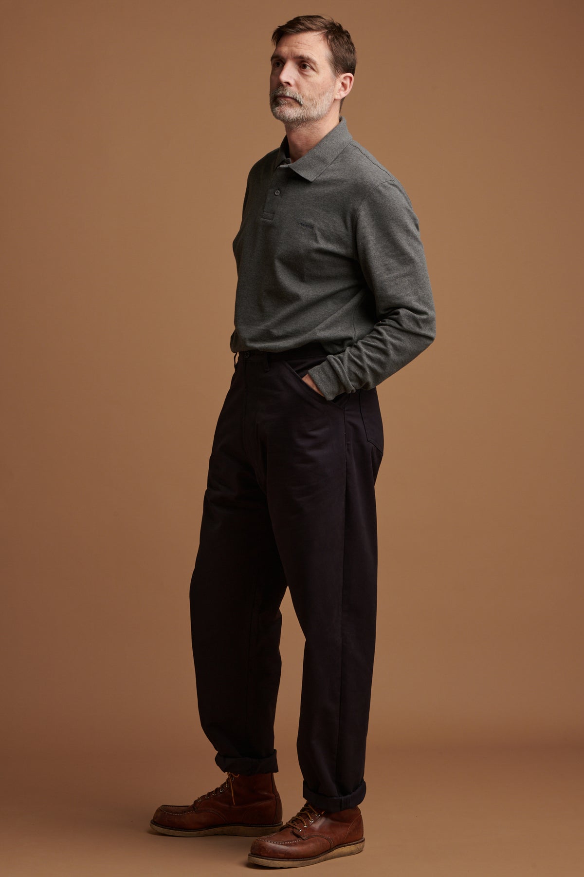 Patrick Grant wearing cotton chore trousers in navy with the hem rolled up. Worn with long sleeve polo shirt in grey.