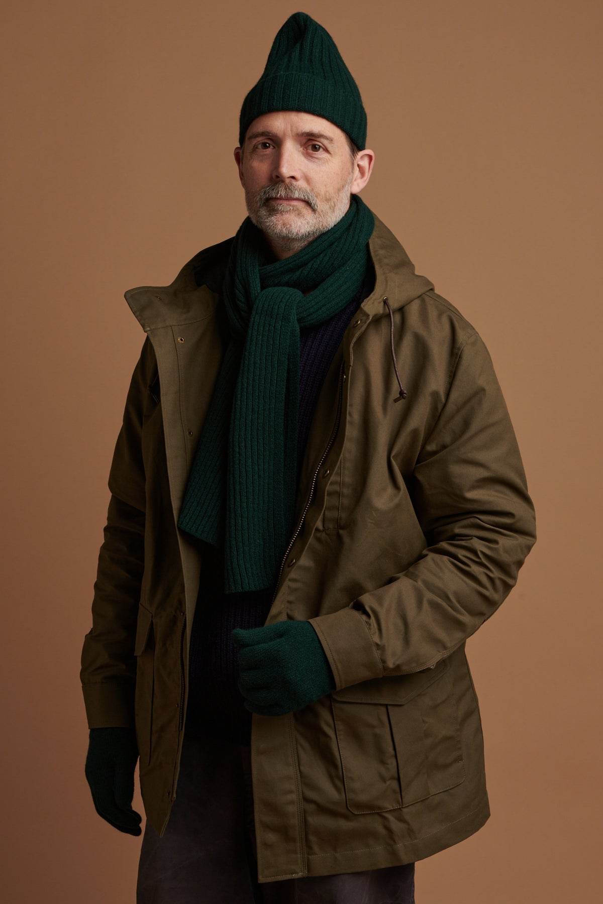 
            Patrick Grant wearing lambswool beanie hat, scarf and glove in bottle green with waxed mountain parka in olive