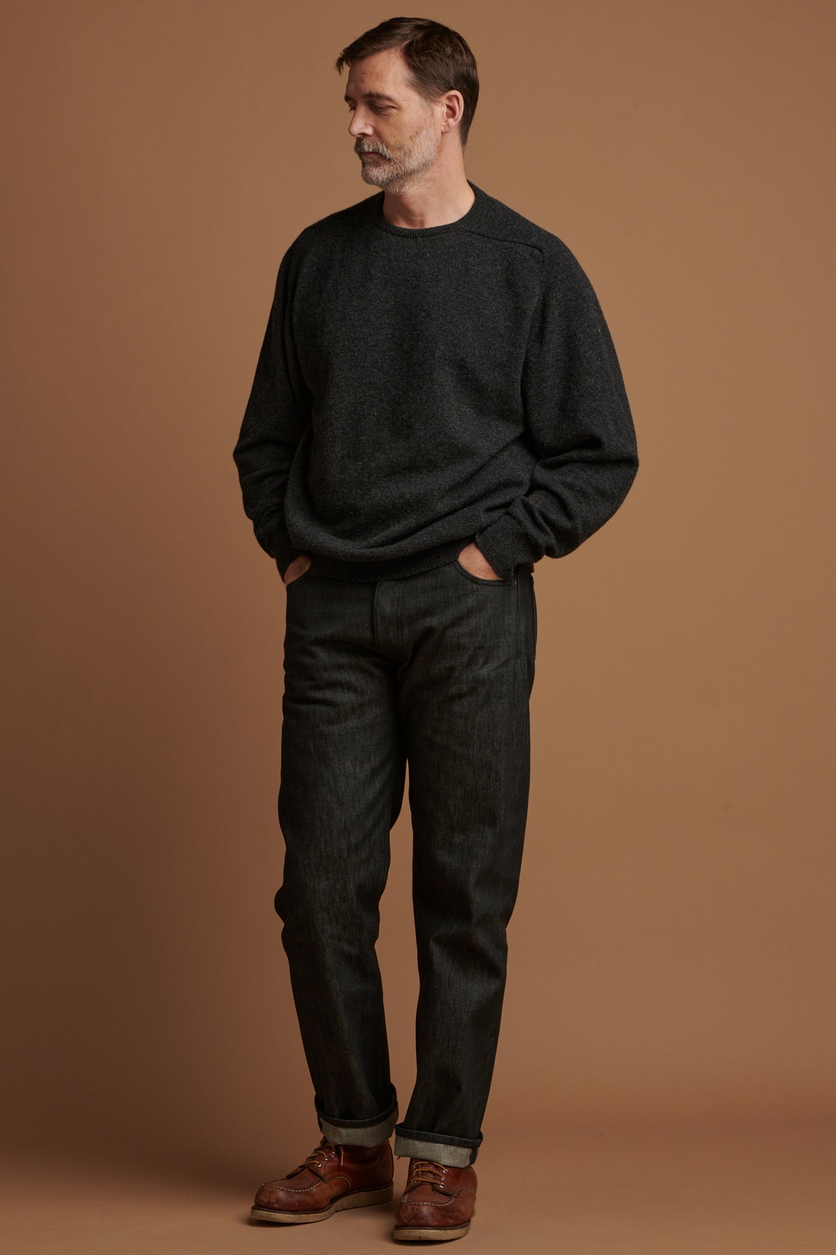 
            Patrick Grant wearing Community Clothing loose fit button fly Arran jean in black with the hem rolled up paired with lambswool saddle shoulder crew neck in charcoal