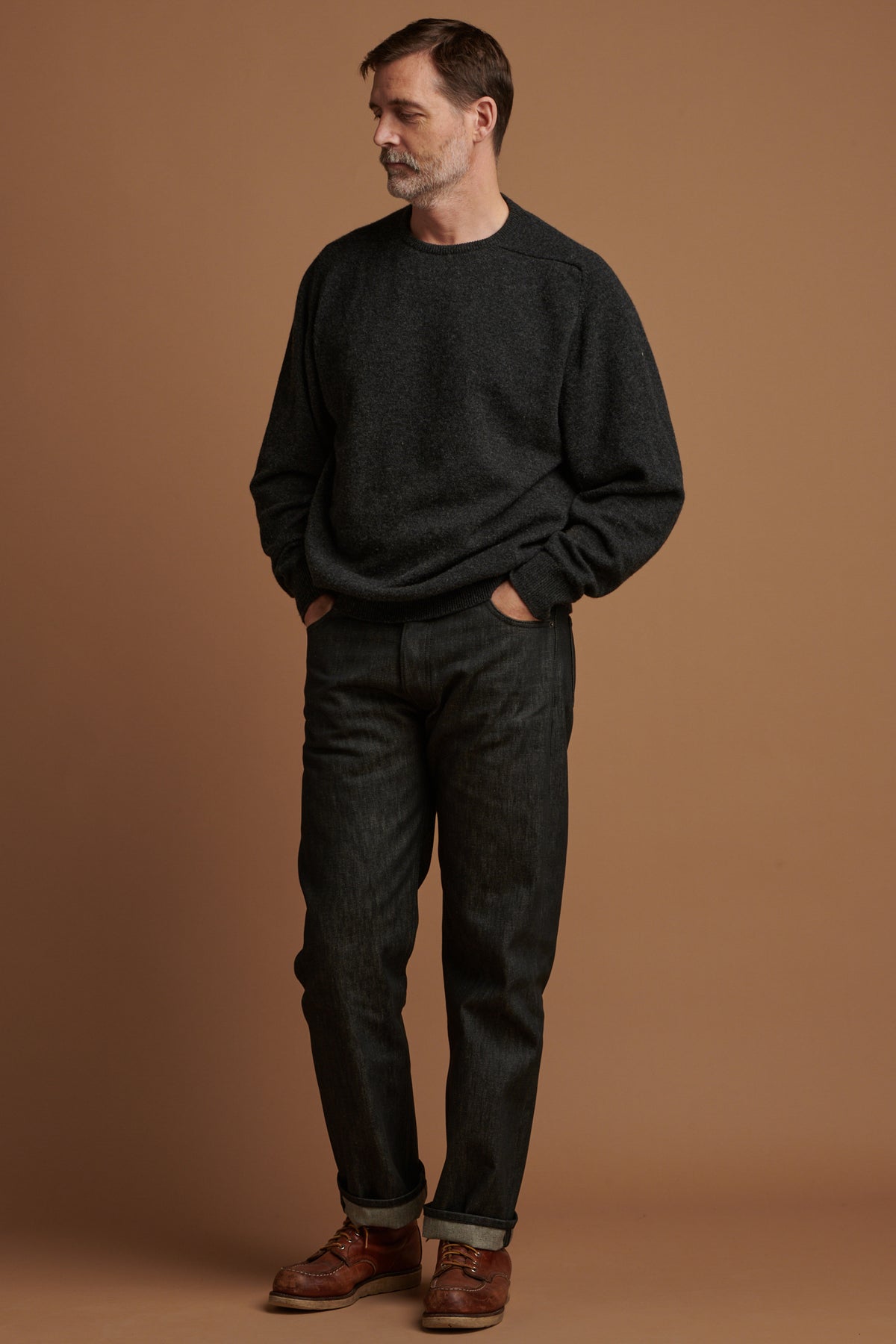 Patrick Grant wearing Community Clothing loose fit button fly Arran jean in black with the hem rolled up paired with lambswool saddle shoulder crew neck in charcoal