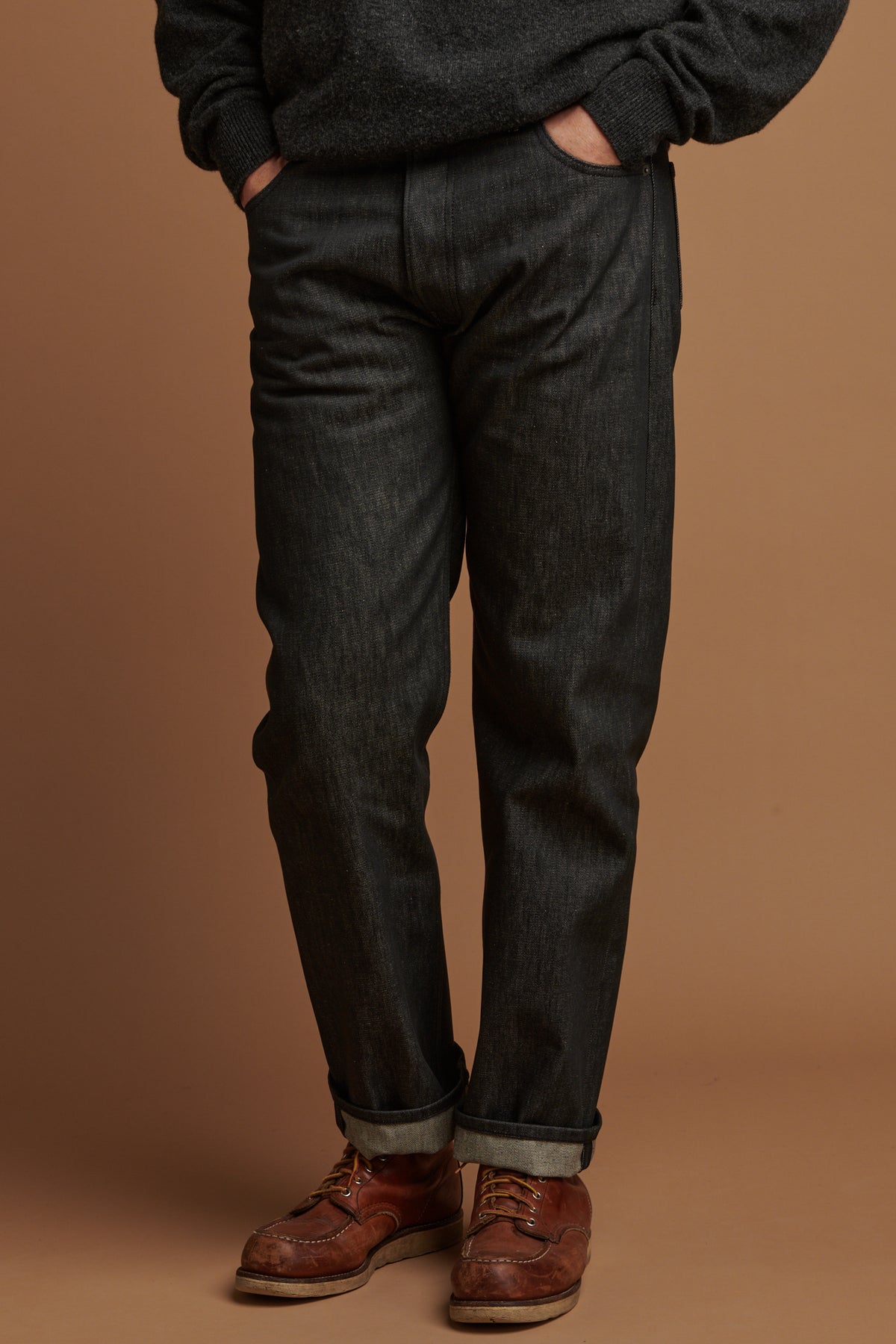 Waist down of Patrick wearing loose fit button fly Arran jean in black with rolled hem.