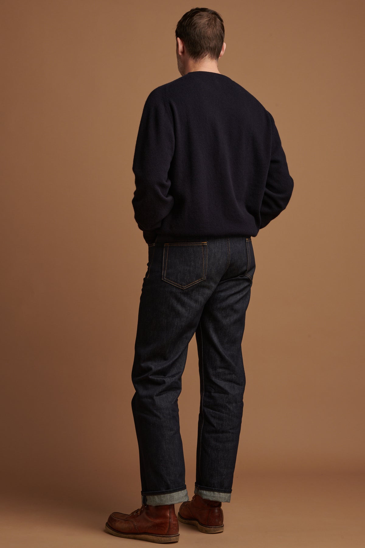 The back of Patrick wearing loose fit button fly Arran jean in indigo with the hem rolled up, paired with lambswool saddle shoulder crew neck in navy.