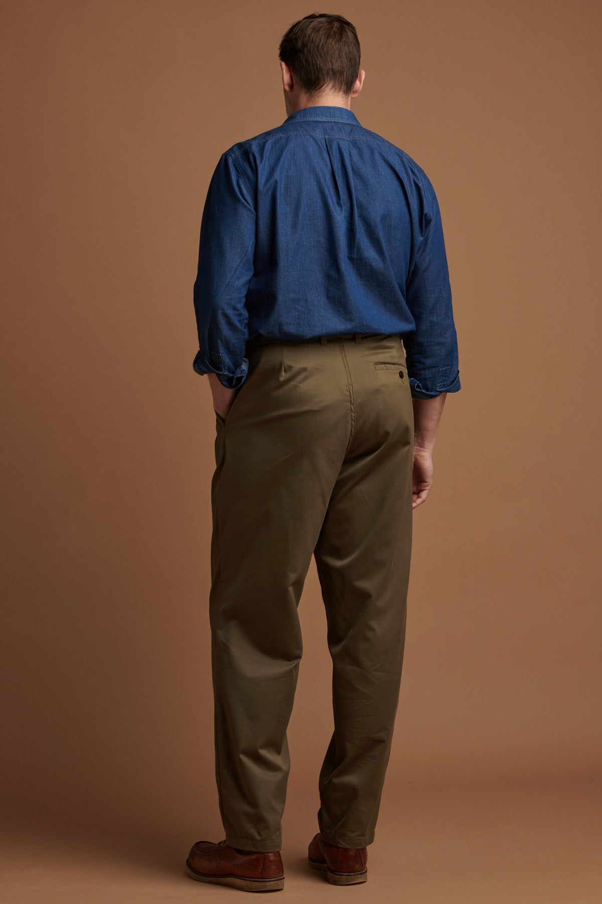 The back of male wearing pleated cotton chino in olive with one back pocket with button fastening