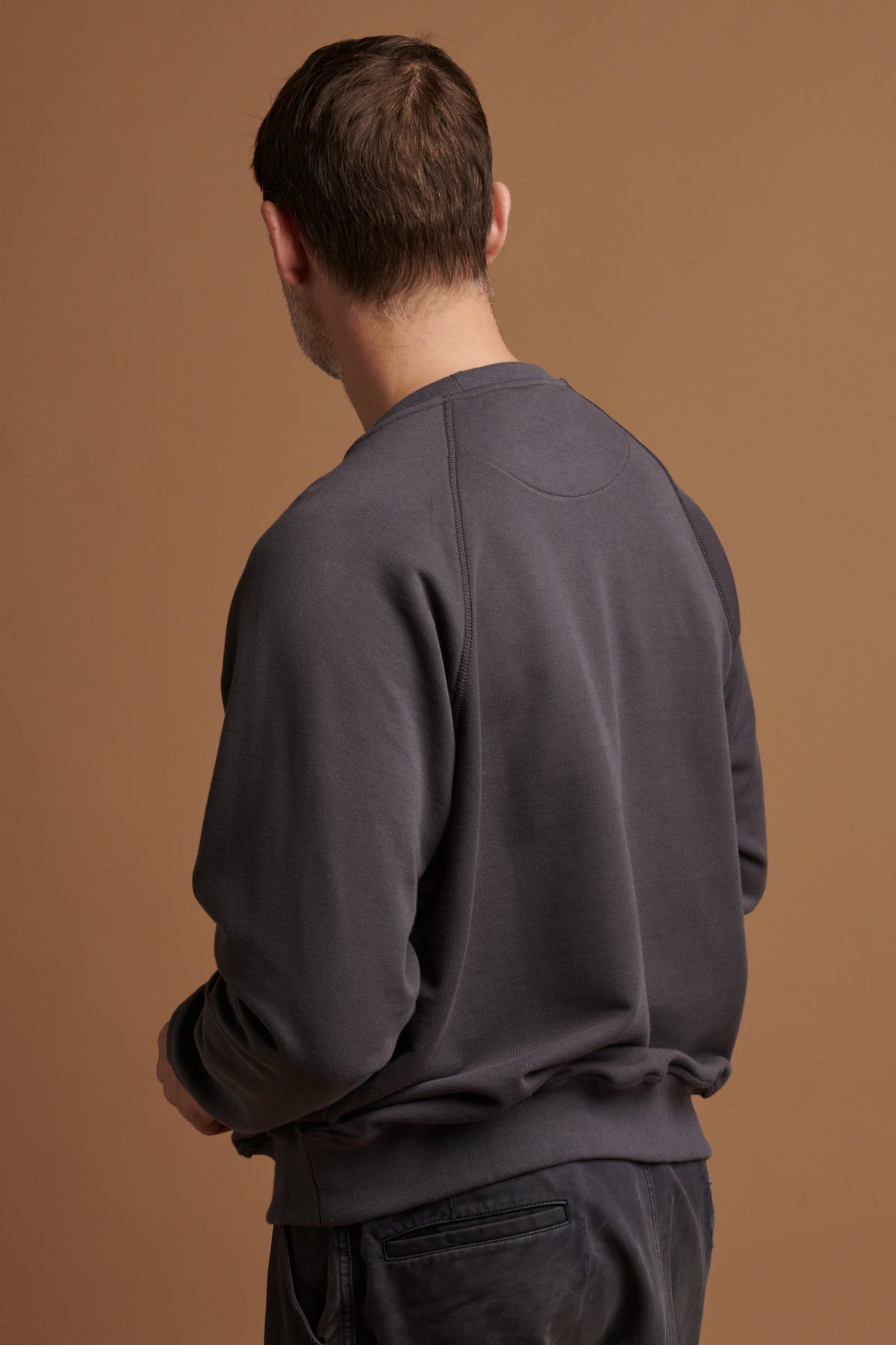 
            The back of Patrick wearing organic cotton raglan sweatshirt in slate grey