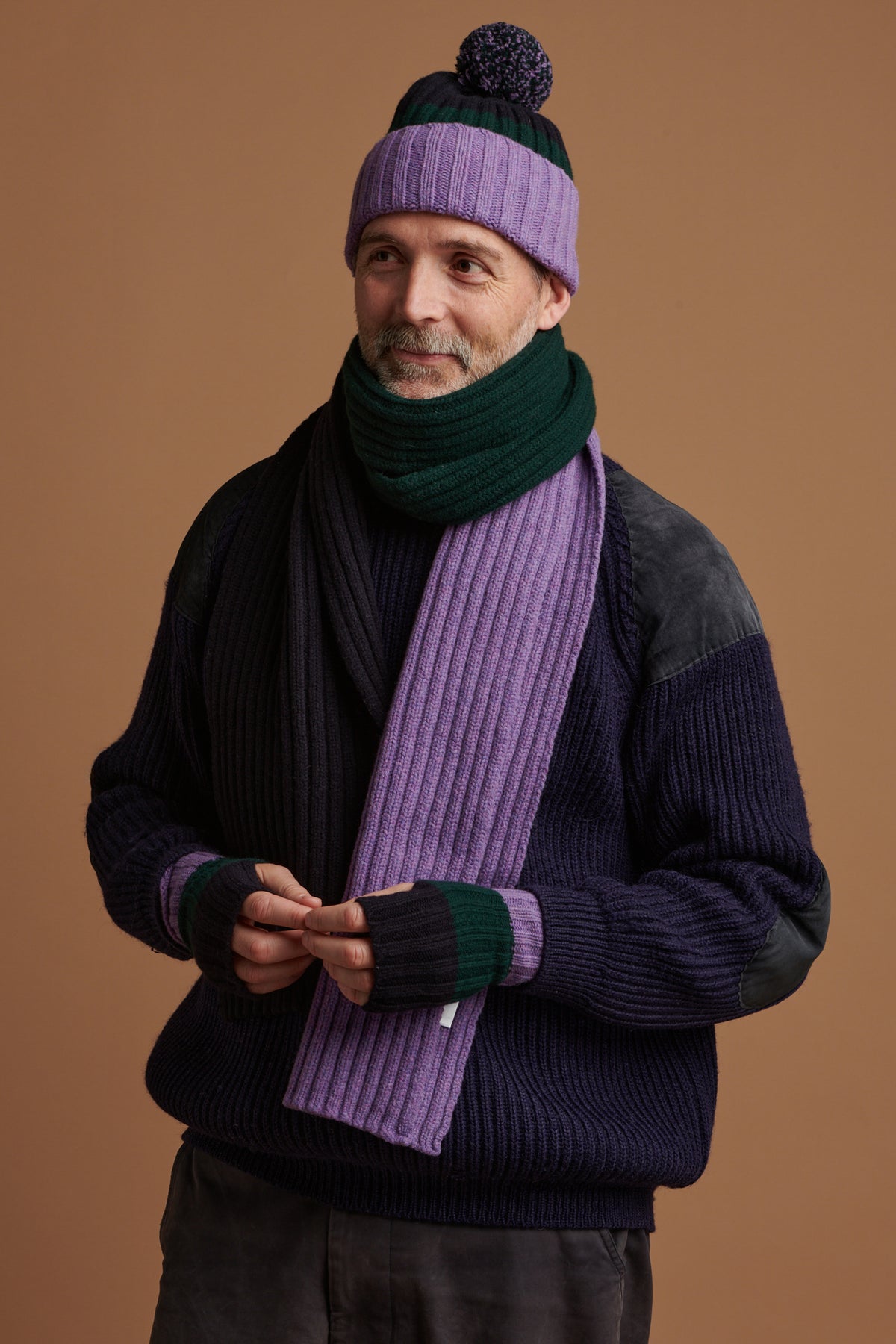 
            Patrick Grant wearing stripe hat scarf and fingerless gloves in green, navy and purple with lambswool fisherman ribbed jumper in navy