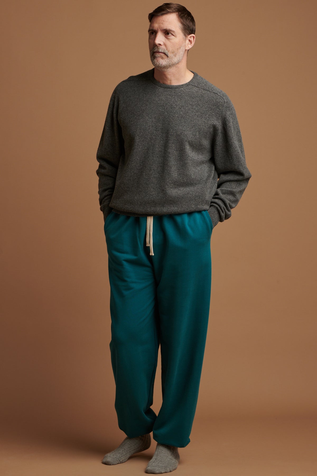 Patrick wearing men's sweatpants in teal paired with lambswool saddle shoulder crew neck in grey and alpaca bed socks in grey