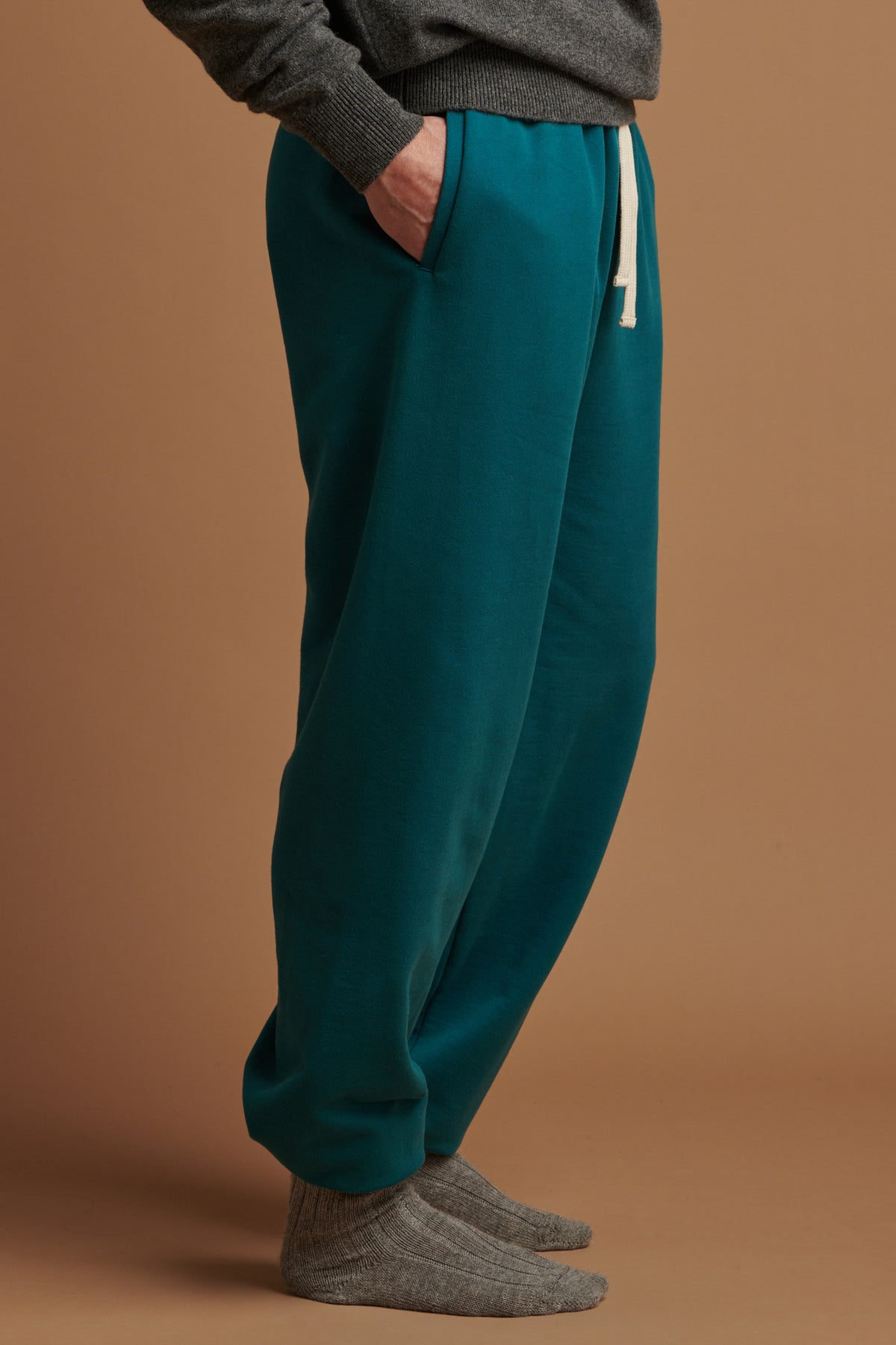 Waist down of male wearing men's sweatpants in teal with his hand in the front pocket and ecru drawcord on show. worn with lambswool saddle shoulder crew neck in grey