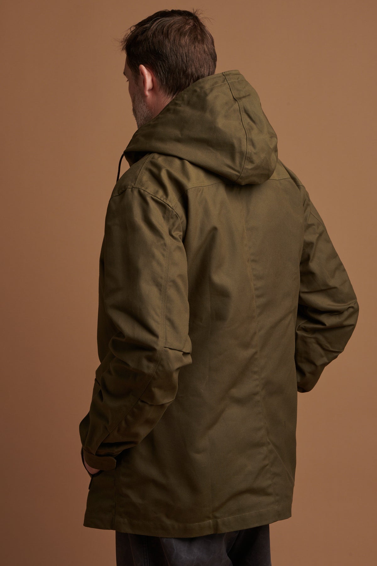 The back of Patrick wearing waxed mountain parka in olive with hood