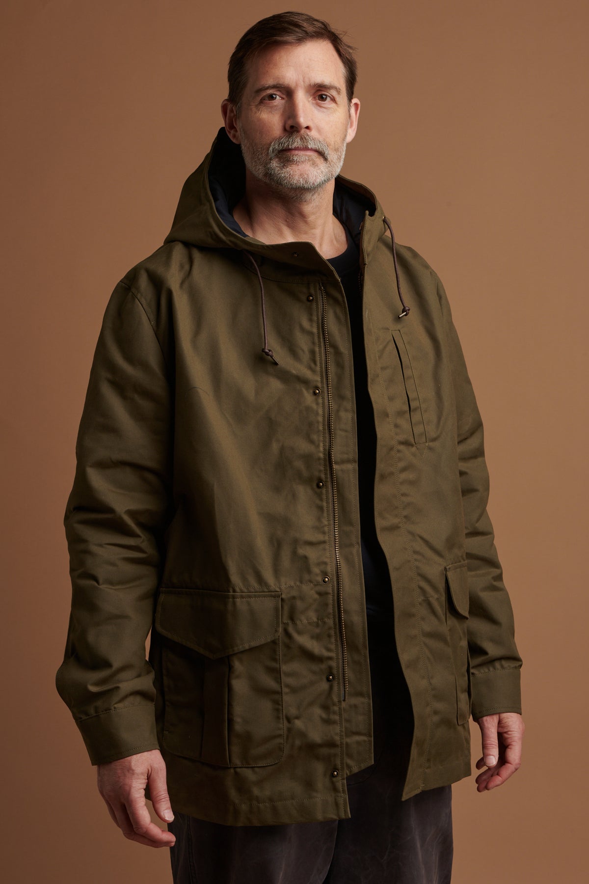 Patrick Grant wearing Community Clothing waxed mountain parka in olive with zip fastening as well as press studs. Three external pockets