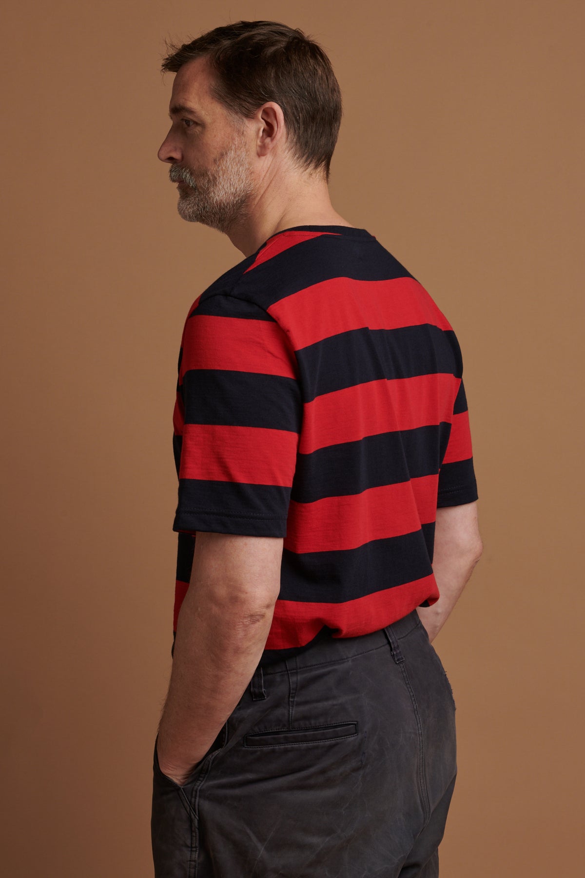 The back of Patrick wearing wide stripe short sleeve t shirt in red and navy tucked into trousers