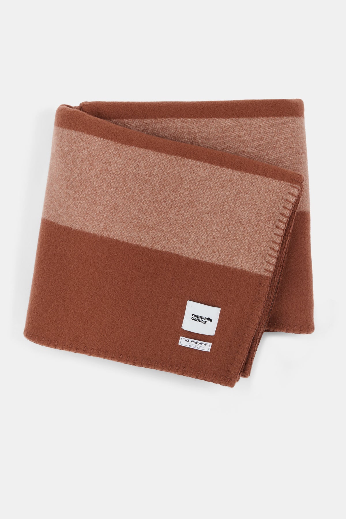 
            Marino blanket in tan dark brown and ecru stripe with Community Clothing woven logo in the bottom right hand corner.