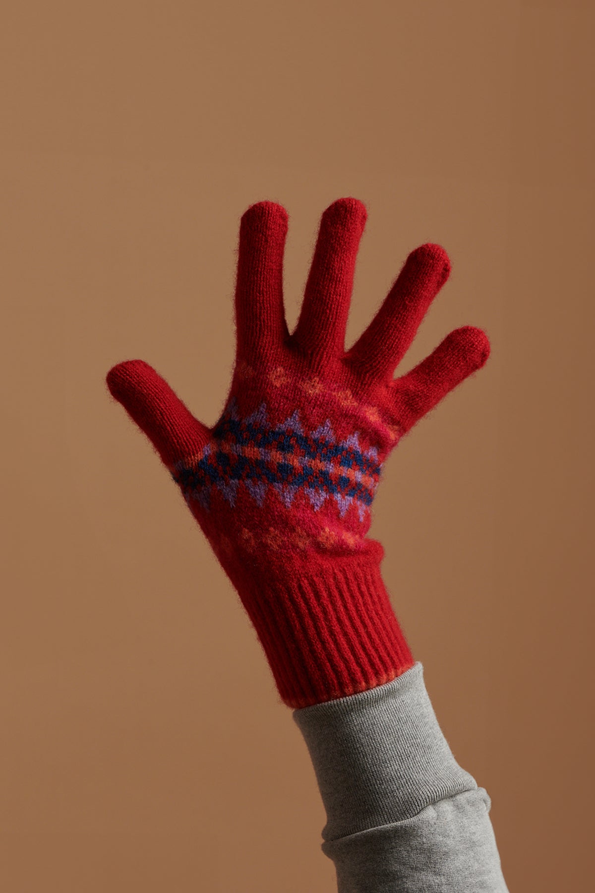 Hand in the air wearing fair isle lamsbwool glove in red with grey sweatshirt