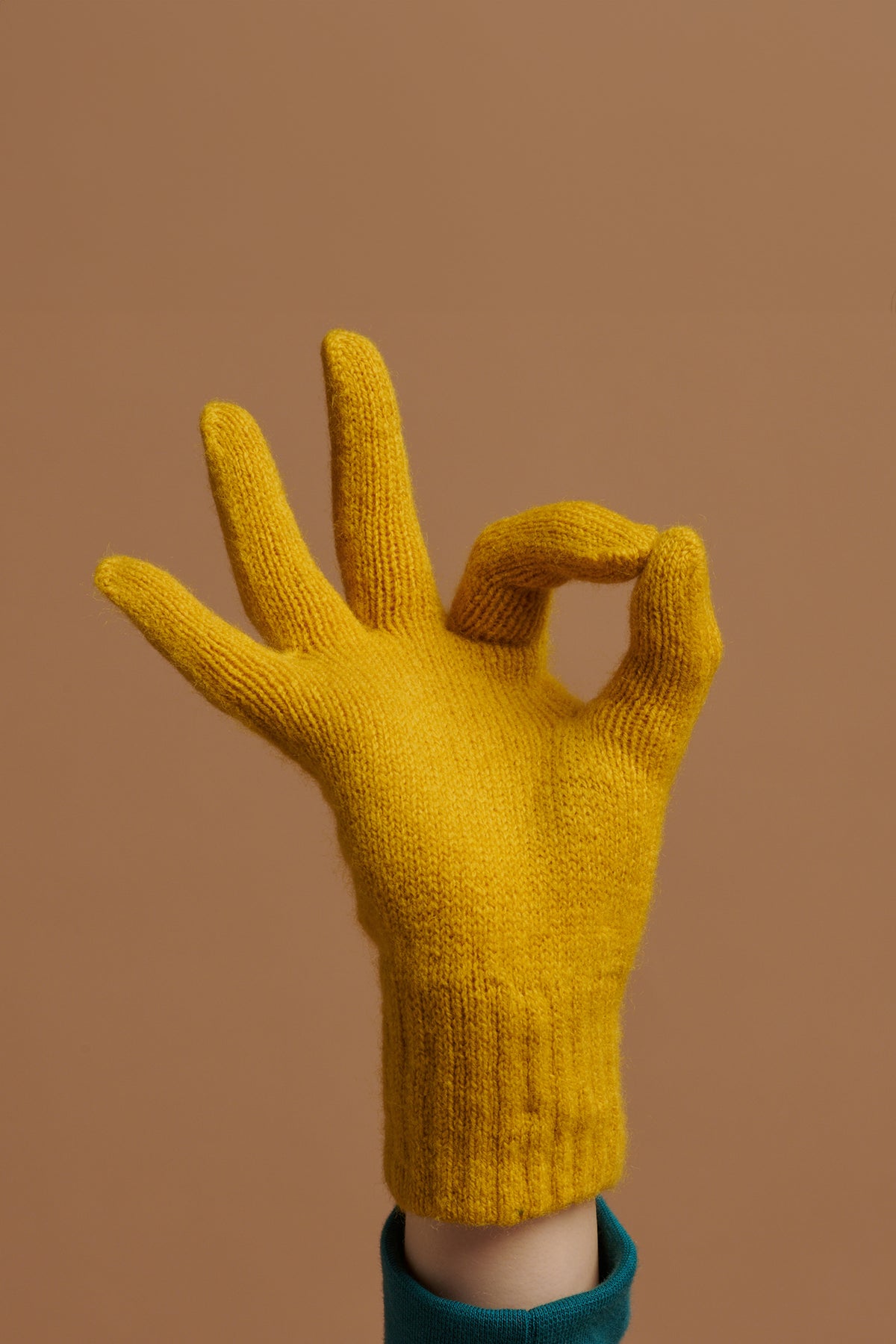 
            Hand wearing lambswool gloves in mustard doing the OK sign