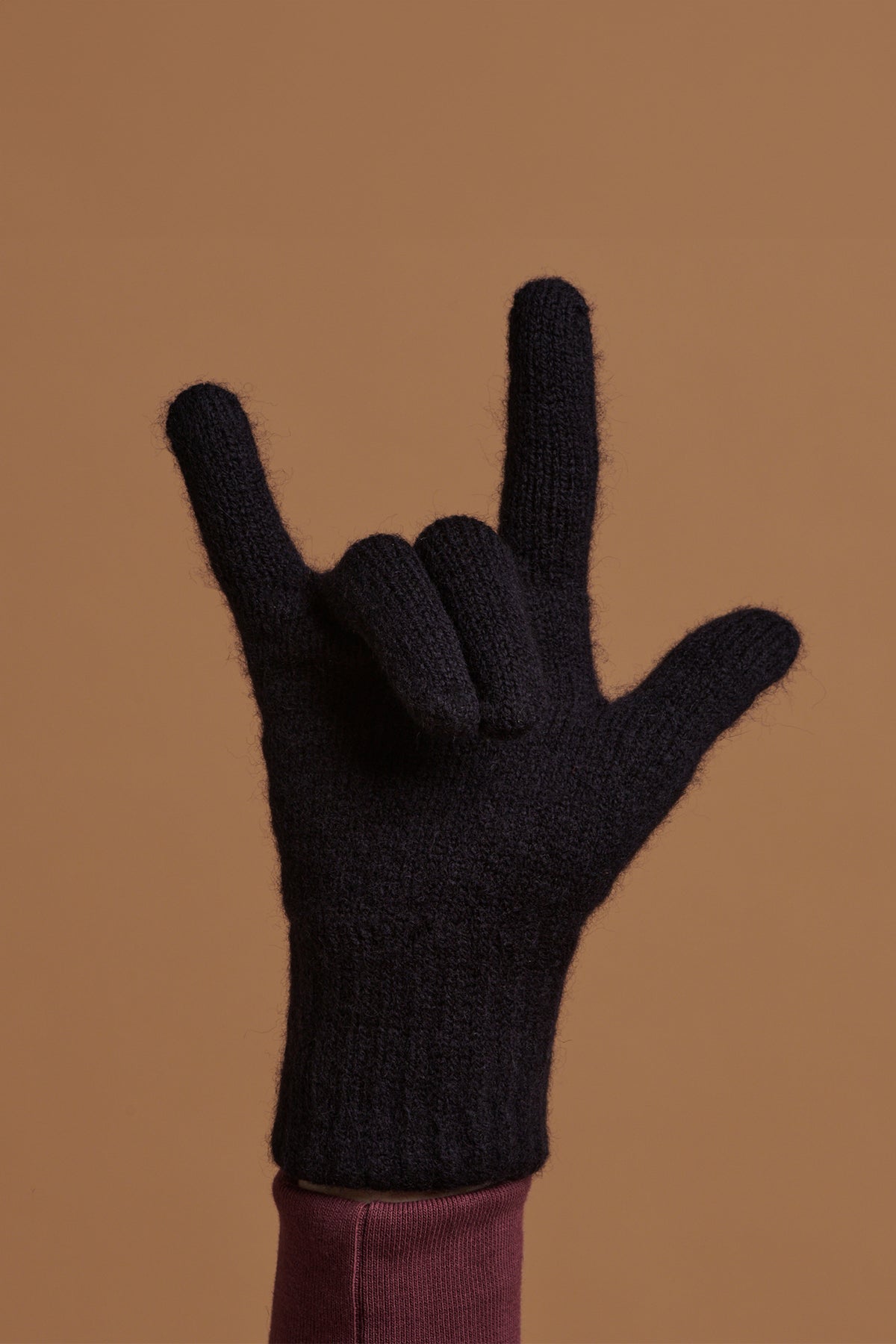 
            Hand wearing navy lambswool gloves holding the &#39;hand horns&#39; or rock hand gesture symbol