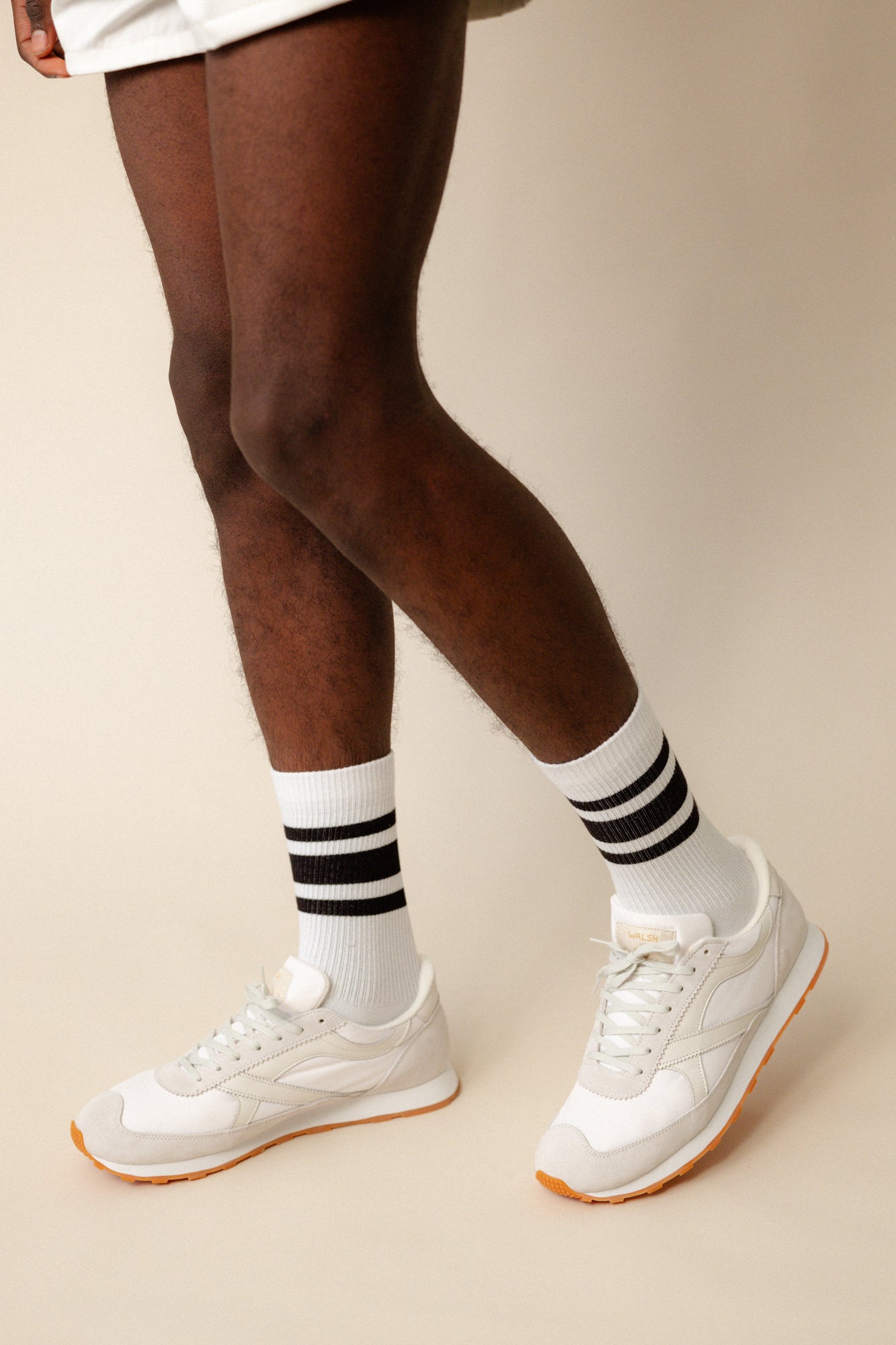 black model wearing calf length sports socks in white with black stripe with white Walsh x Community Clothing Beacon trainers