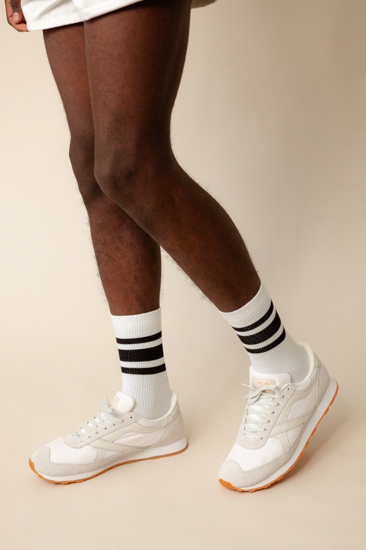 
            black model wearing calf length sports socks in white with black stripe with white Walsh x Community Clothing Beacon trainers