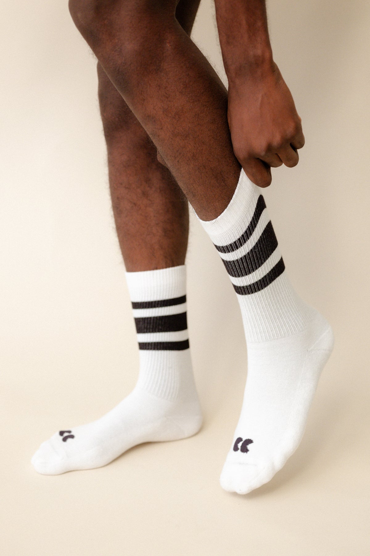 
            black model wearing calf length sports socks in white with black stripe with CC logo on the toe