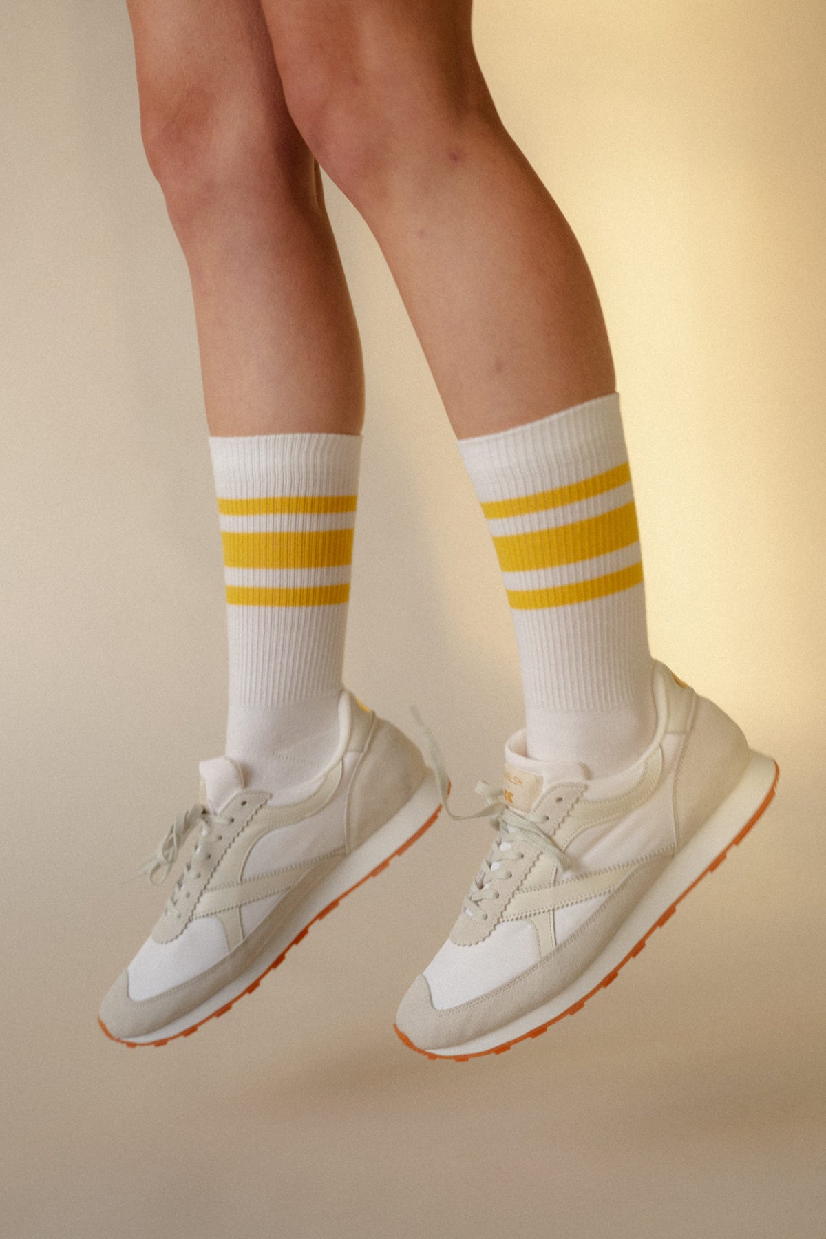 
            white model wearing calf length sports cotton socks in white with yellow stripe, with Walsh x Community Clothing Beacon trainers