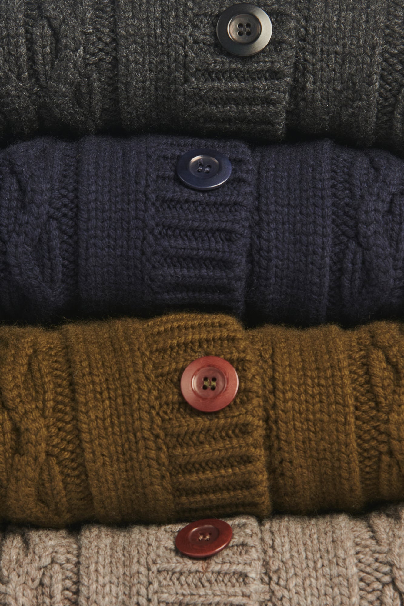 Stack of knitted sweaters in various colors with button details.