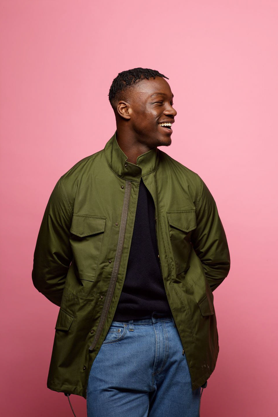 young black male smiling as he is wearing an olive field jacket by community clothing