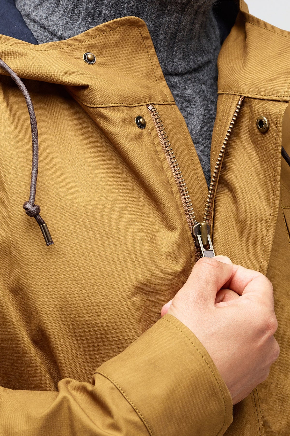 close up of the top of zip of mountain parka in tan, with button poppers. brown draw cord through hood