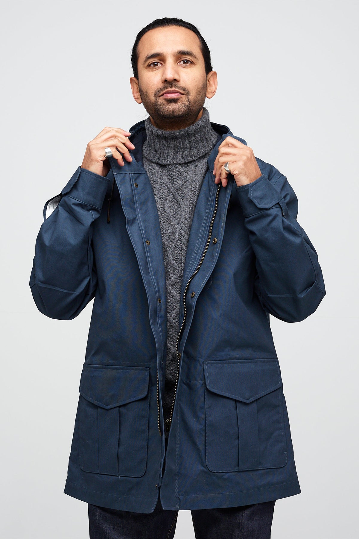 Male wearing mountain parka in navy, unzipped showing popper button fastenings .